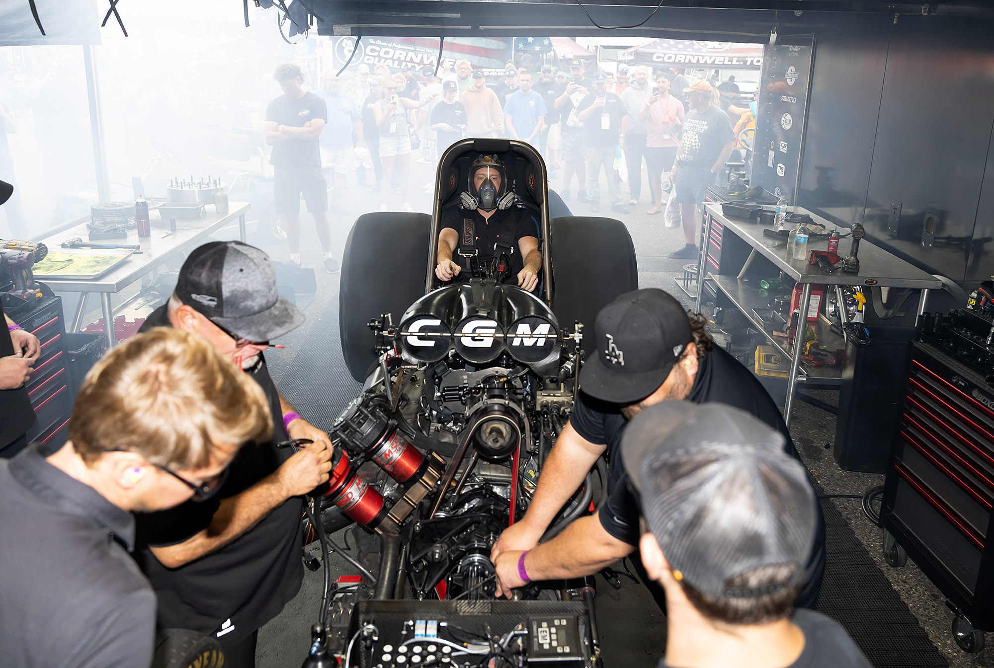 Fans watch through the haze as the CGM crew warms the engine with the driver masked in the car