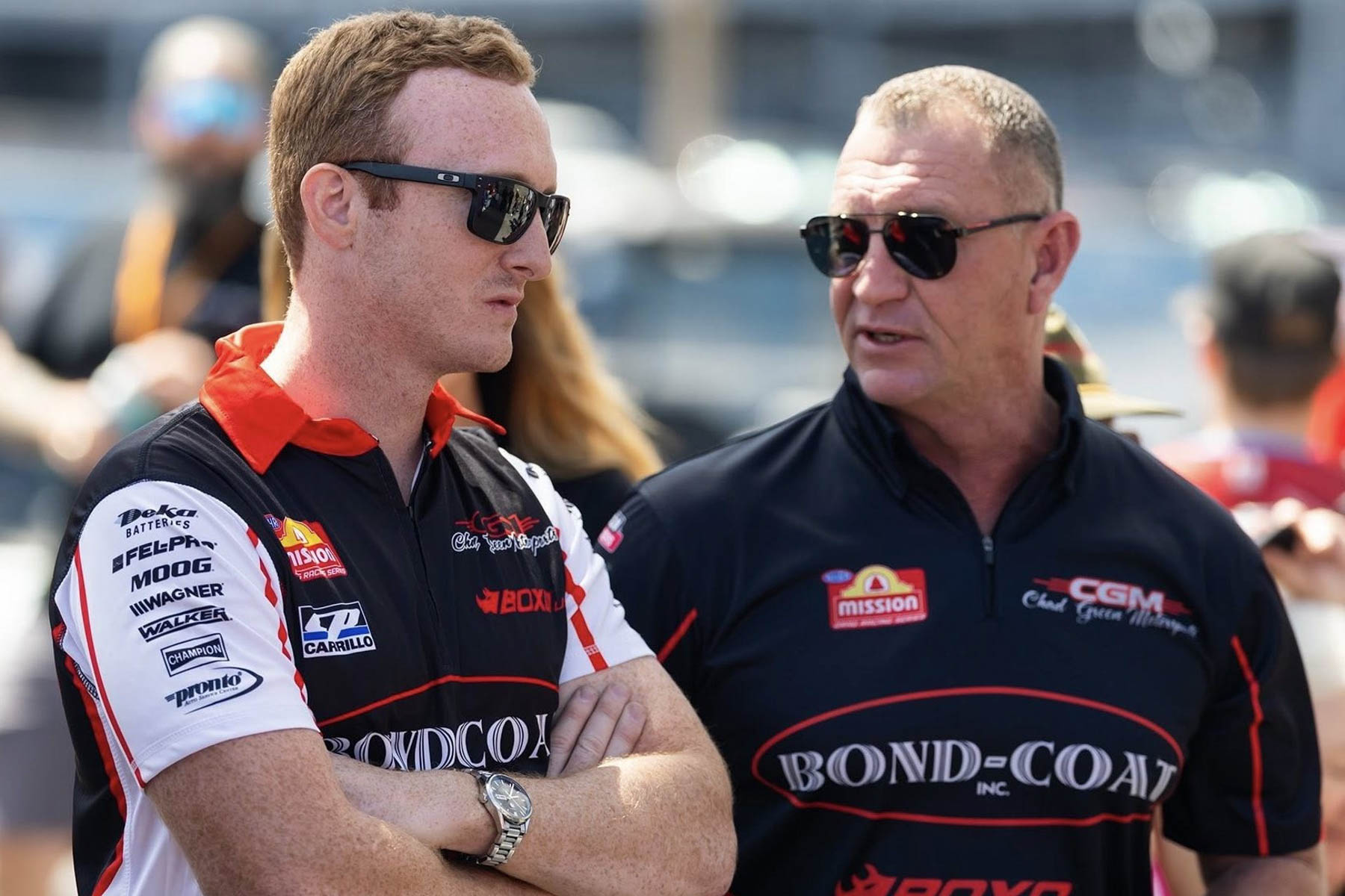 Hunter and Chad Green in team shirts and sunglasses, talking in the pits